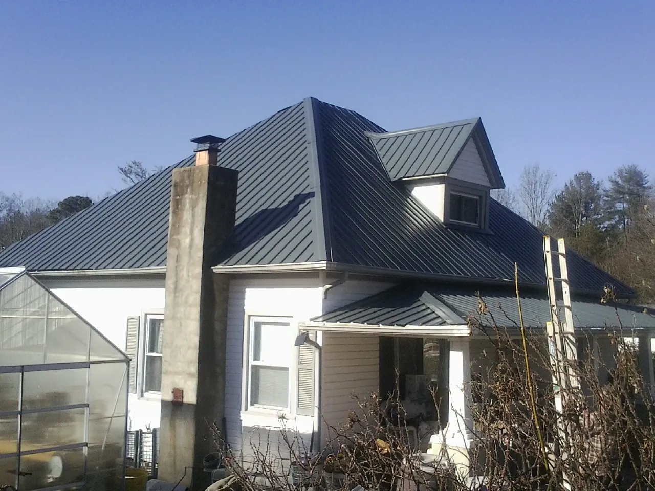 Dark blue standing seam metal roof on a white farmhouse with dormer — Slate & Tile Roof Repair by Roofing Brothers in Woodland Hills