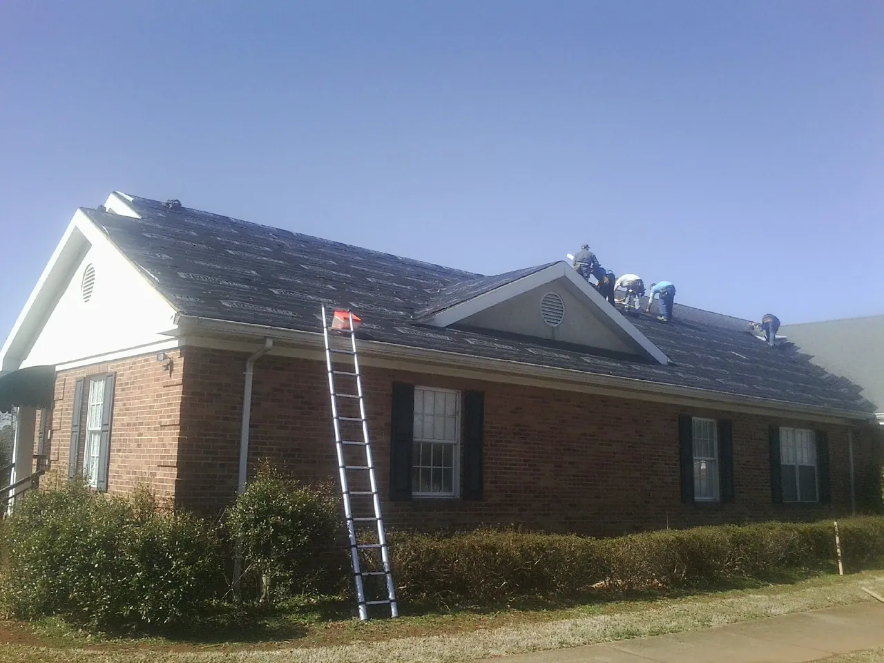 Crew tearing shingles off a brick ranch roof with a ladder set — Emergency Roof Repair work by our crew in Woodland Hills
