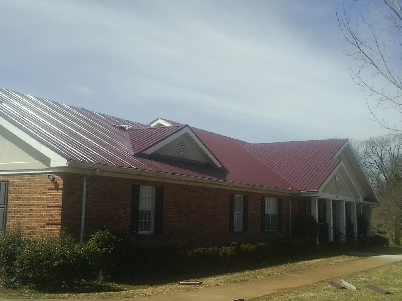 Red metal roof with gabled entries on a long brick building, from a Hail Damage Roof Repair job in Woodland Hills