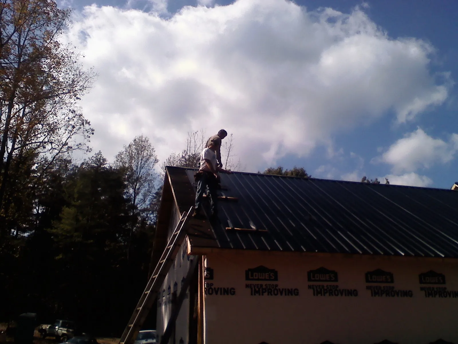 Roofer fastening dark metal panels high against a cloudy sky, from a Roof Inspection job in Woodland Hills