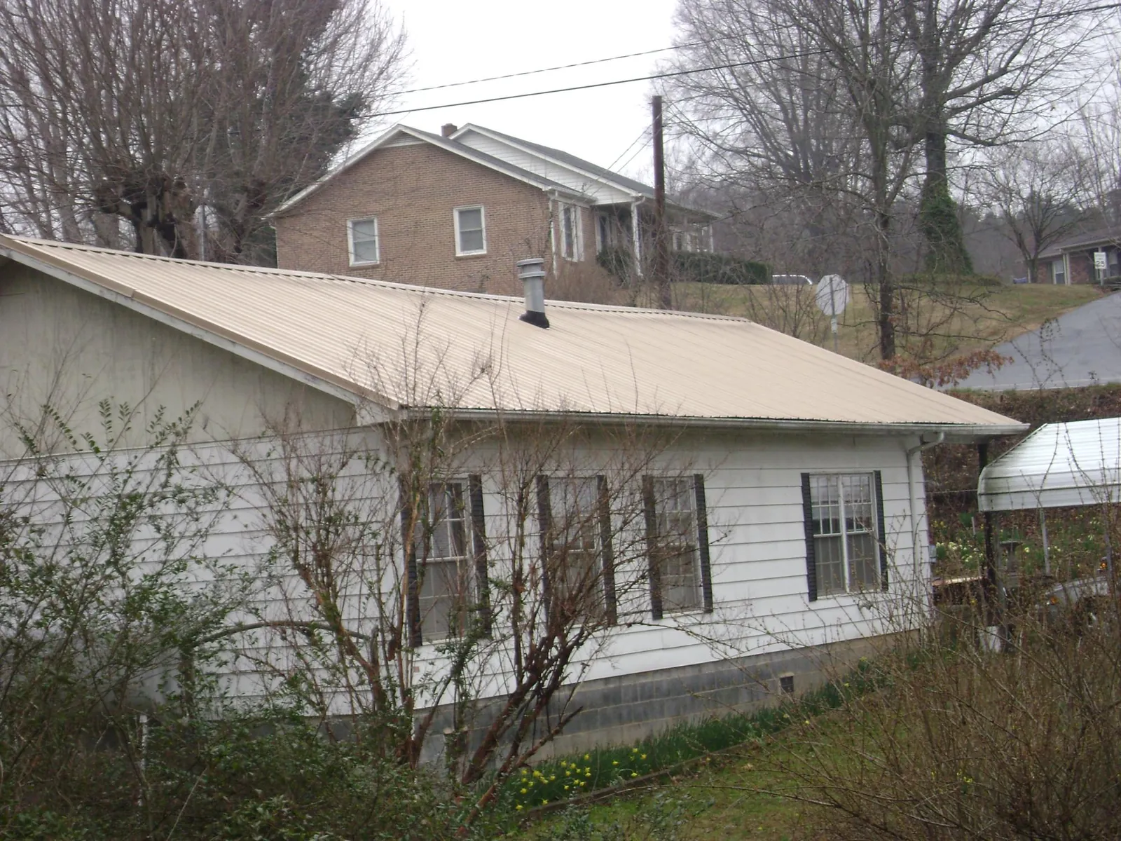 Tan metal roof on a white sided house set into a hillside — Commercial Roofing by Roofing Brothers in Woodland Hills