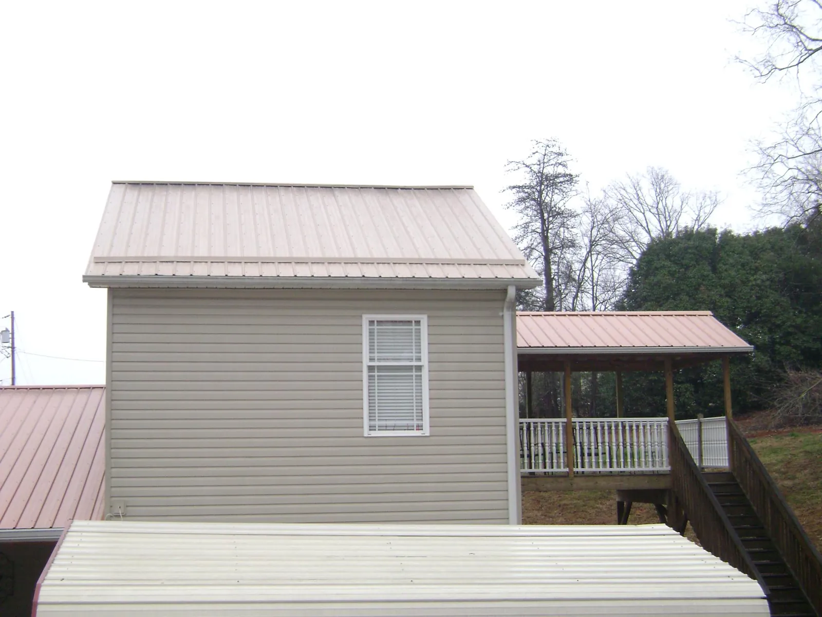 Tan metal roofs on a two story addition and attached porch, from a Roof Replacement job in Woodland Hills